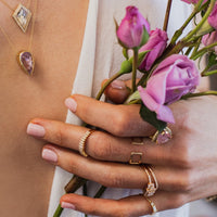 Close-up of a person wearing jewelry with pink flowers in the background