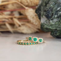 Gold ring with green gemstones on a neutral background with decorative elements