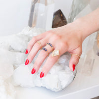 hand with red fingernails resting on quartz cluster wearing 5 18kt gold rings with sapphires and diamonds