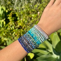 Assorted beaded bracelets in blues and aqua on an arm.