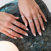 Close-up of hands wearing multiple white gold and diamond rings on a labradorite stone