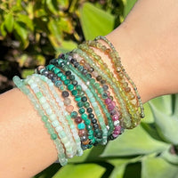 Multicolored green beaded bracelets on a wrist with a green leafy background