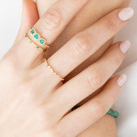 Close-up of a woman's hands wearing multiple rings with green gemstones on a blurred background.