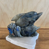 Stylized labradorite sculpture of two dolphins on a wooden surface