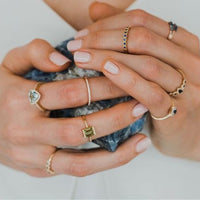 Close-up of hands wearing multiple gold rings with blue and green gemstones on a neutral background