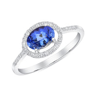 A tanzanite and diamond ring with an 18k white gold band, featuring a central oval tanzanite surrounded by a halo of round diamonds with additional diamonds down the shank.