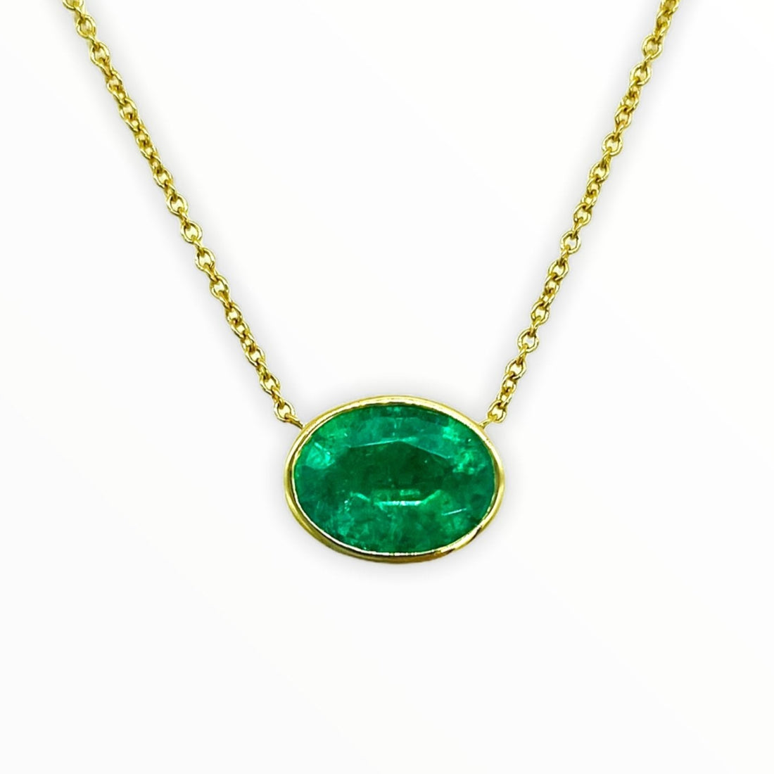 gold necklace with bright oval-shaped, bezel-set faceted emerald gemstone