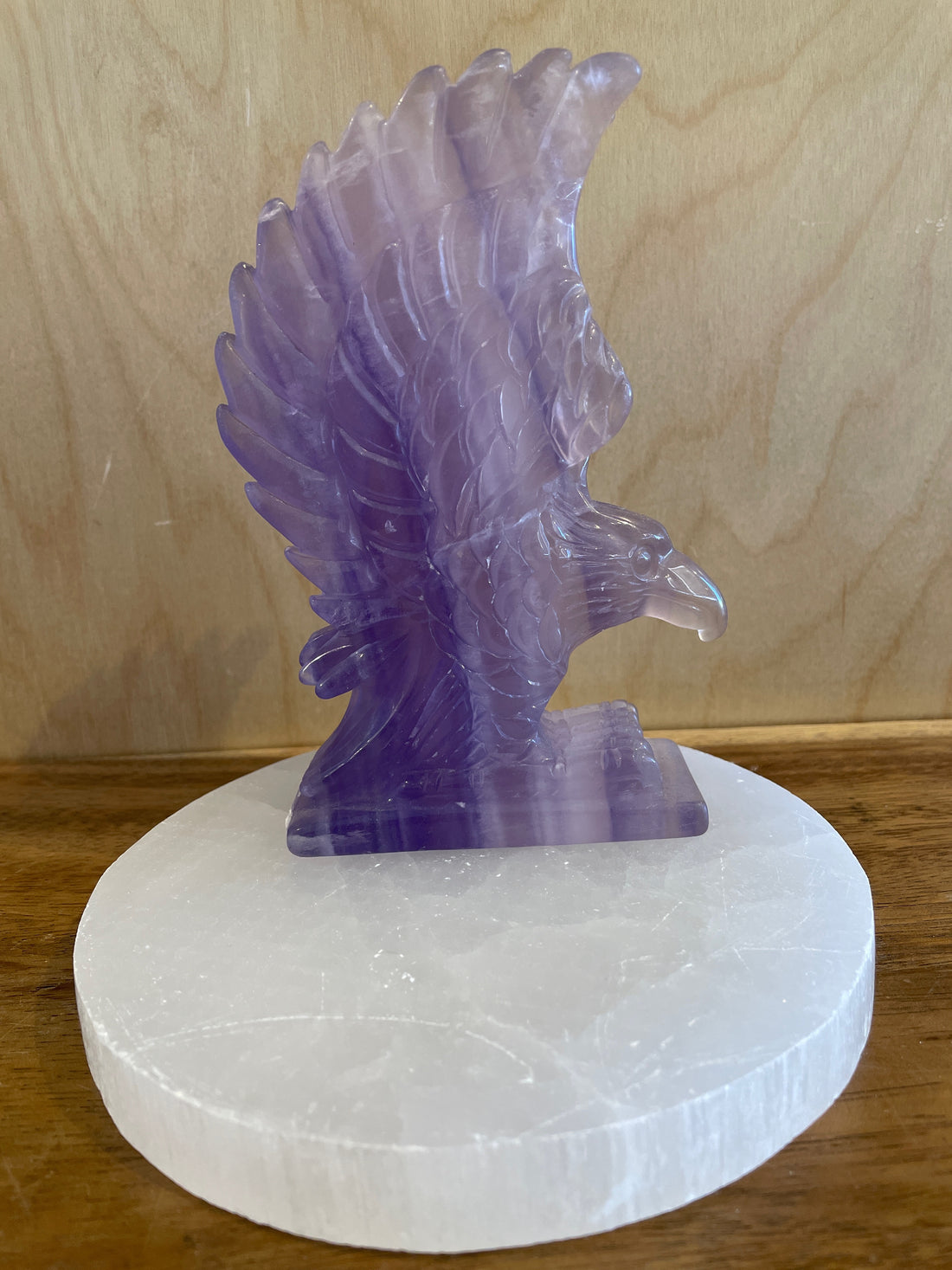 Purple fluorite crystal eagle sculpture on a white marble base against a wooden background