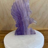 Purple fluorite crystal eagle sculpture on a white marble base against a wooden background