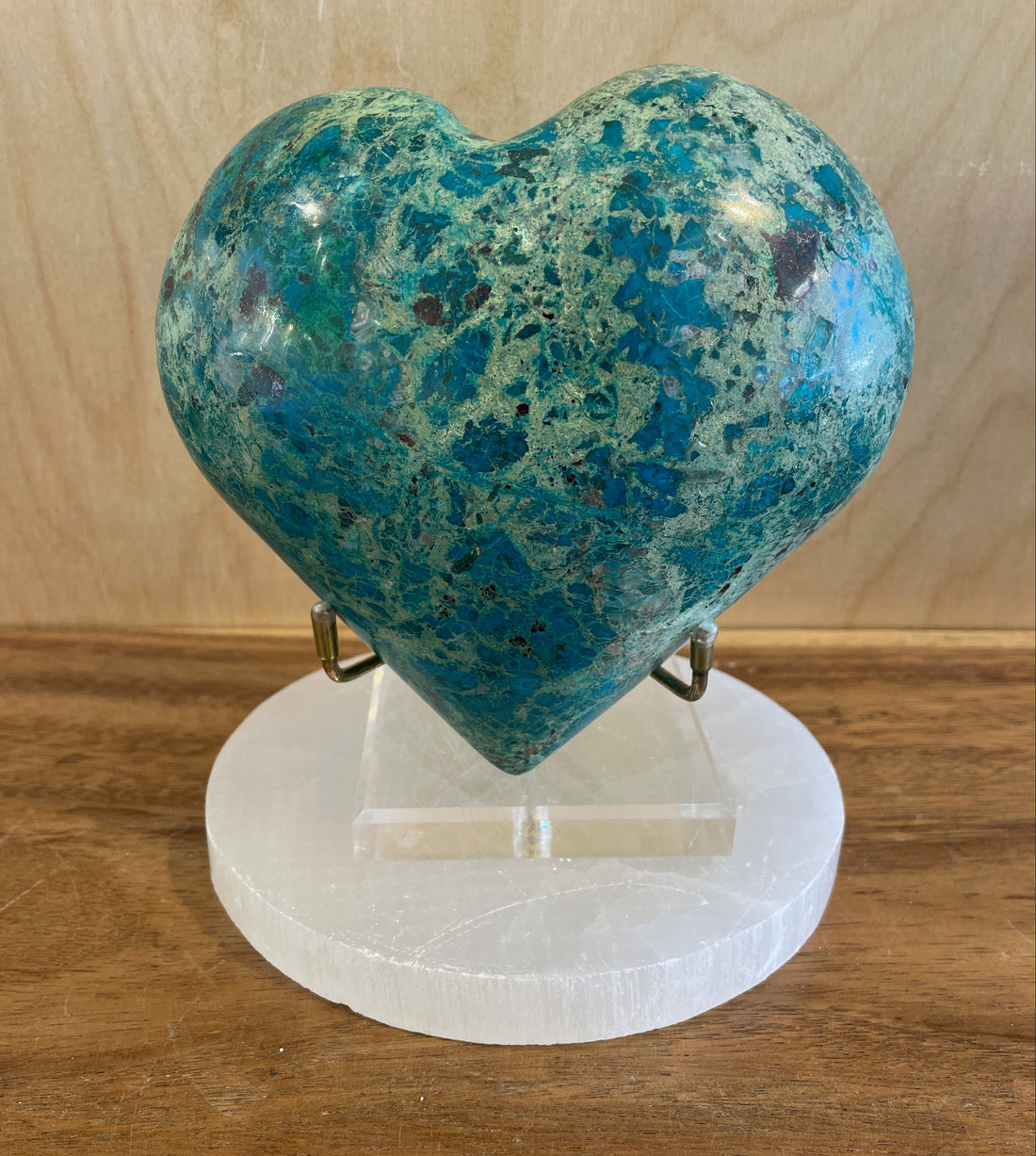 Heart-shaped blue-green chrysocholla on a white stand against a wooden background
