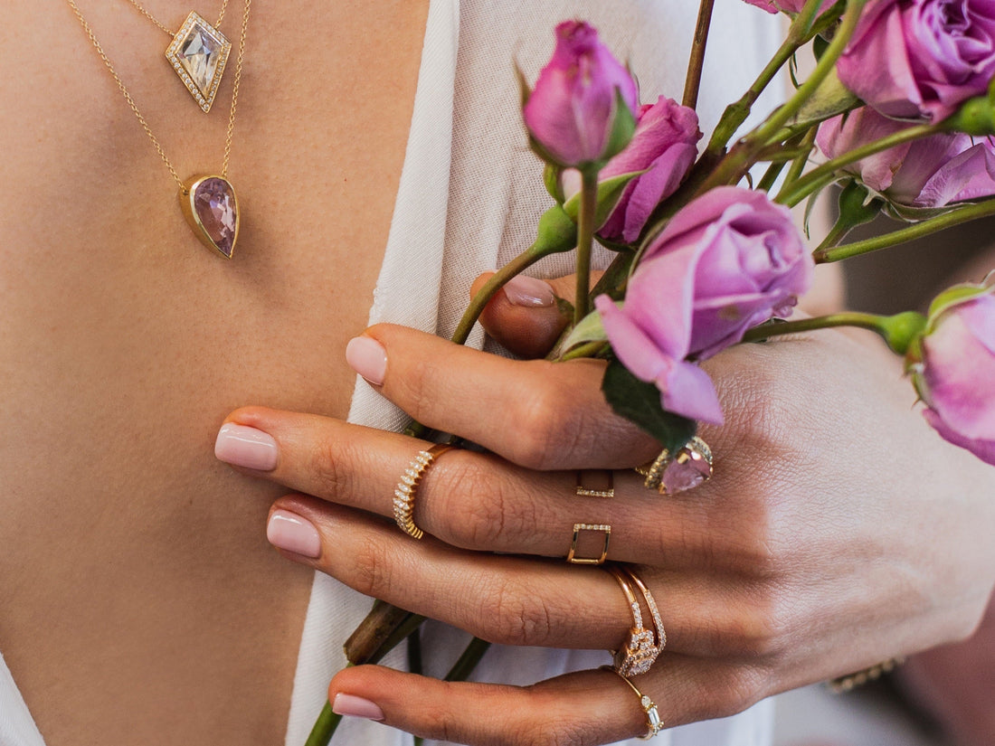 Close-up of a person wearing jewelry with pink flowers in the background