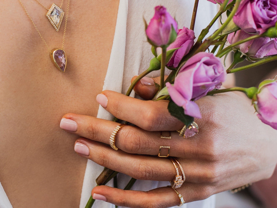 Close-up of a person wearing jewelry with pink flowers in the background
