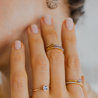 Close-up of a hand with multiple rings and an earring with amethyst stones, blurred background