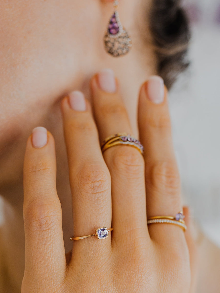 Close-up of a hand with multiple rings and an earring with amethyst stones, blurred background