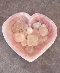 Heart-shaped pink quartz bowl filled with smaller pink quartz hearts on a gray tiled floor