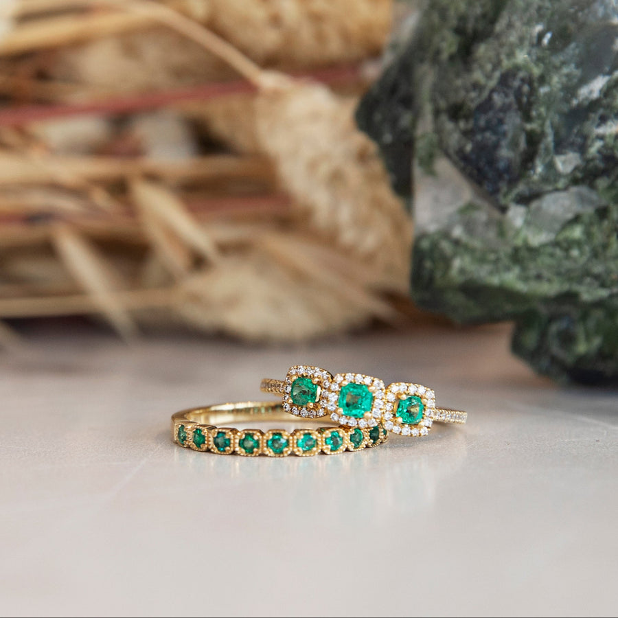 Gold ring with green gemstones on a neutral background with decorative elements