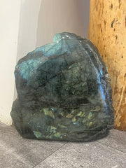 Large labradorite crystal on a concrete floor with a wooden post in the background