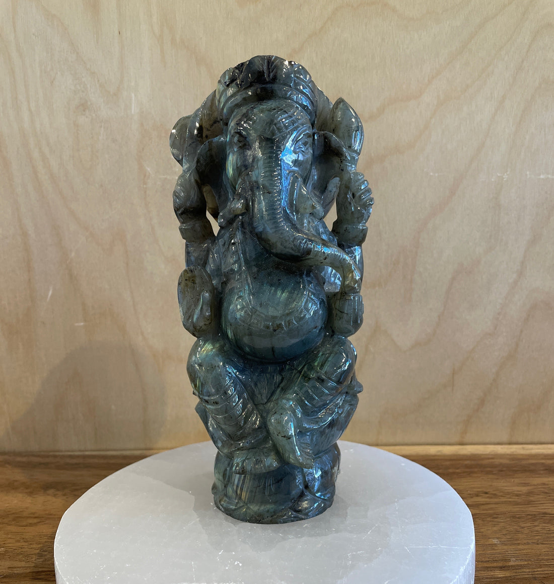 Labradorite statue of a Ganesha deity on a white selenite base against a wooden background
