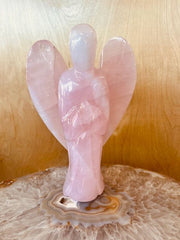 Pink quartz angel figurine on a decorative stone base with a wooden background