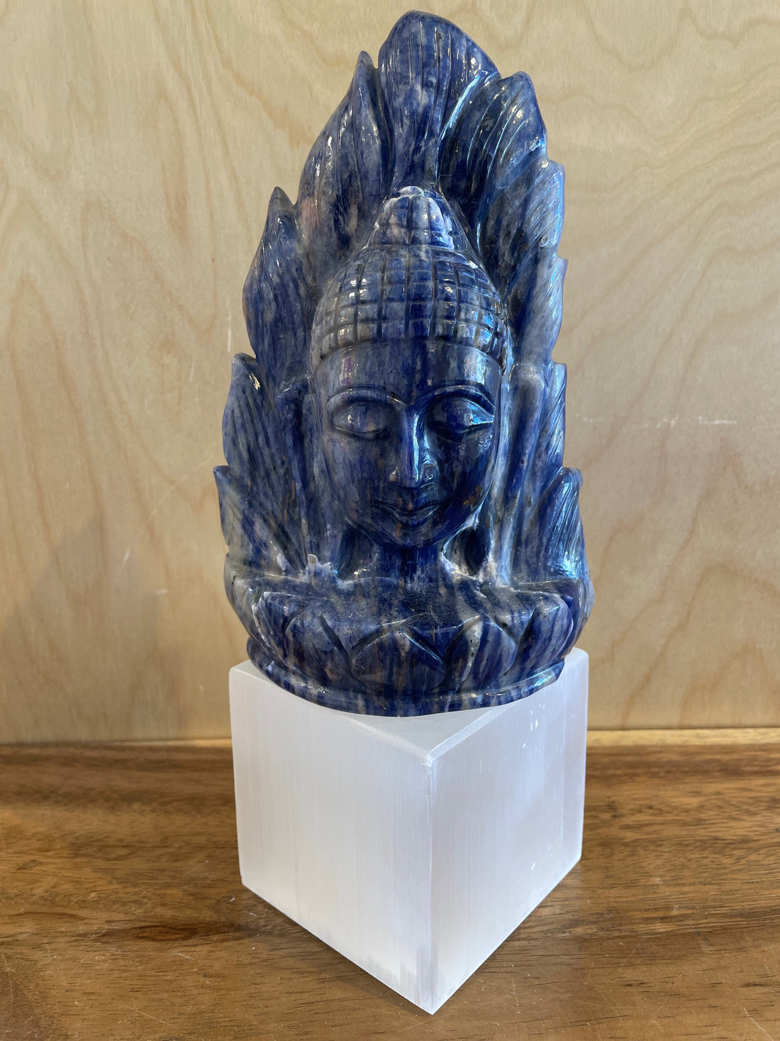 Blue sodalite sculpture of Buddha on a white base against a wooden background