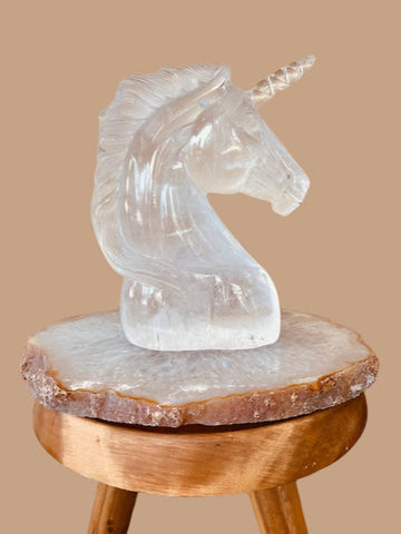 Clear crystal unicorn sculpture on a wooden stool against a beige wall.