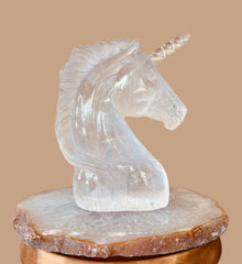 Clear crystal unicorn sculpture on a wooden stool against a beige wall.