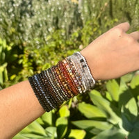 Wrist wearing multiple beaded bracelets with a green outdoor background