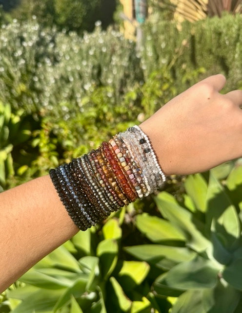 Wrist wearing multiple beaded bracelets with a green outdoor background