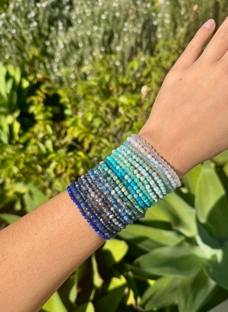 Assorted beaded bracelets in blues and aqua on an arm.