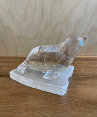 Clear quartz seal figurine on a white base against a wooden background