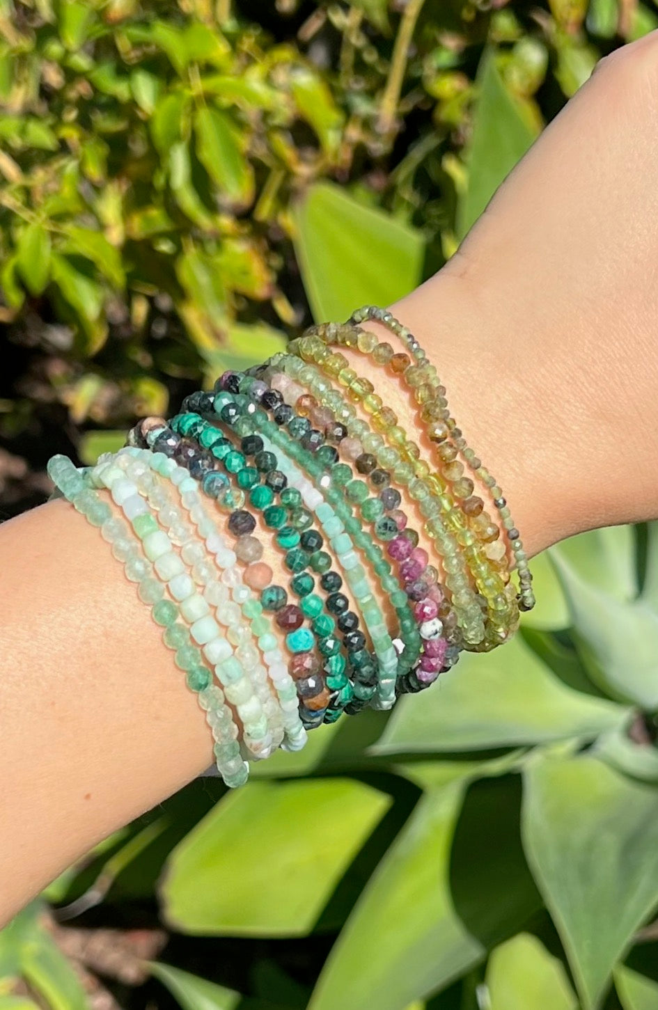Multicolored green beaded bracelets on a wrist with a green leafy background