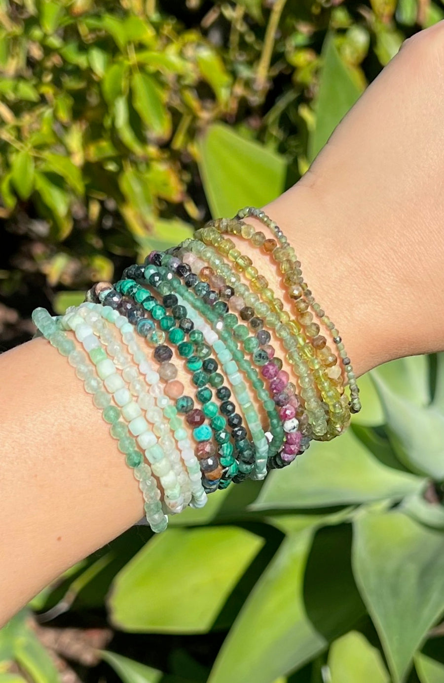 Multicolored green beaded bracelets on a wrist with a green leafy background