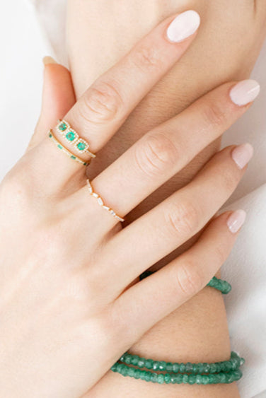 Close-up of a woman's hands wearing multiple rings with green gemstones on a blurred background.