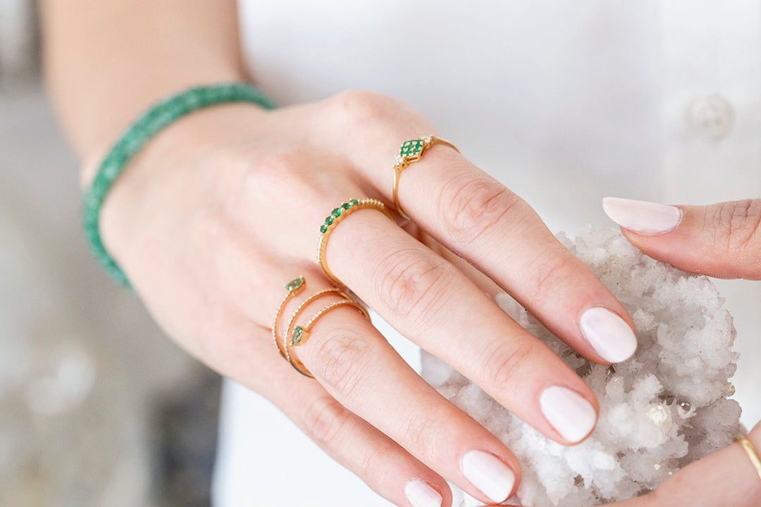 Close-up of a hand wearing gold rings with green gemstones on a white background