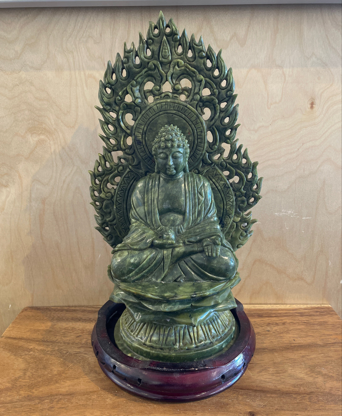 Green Jade Buddha carving with intricate detailing on a wooden base against a wooden background