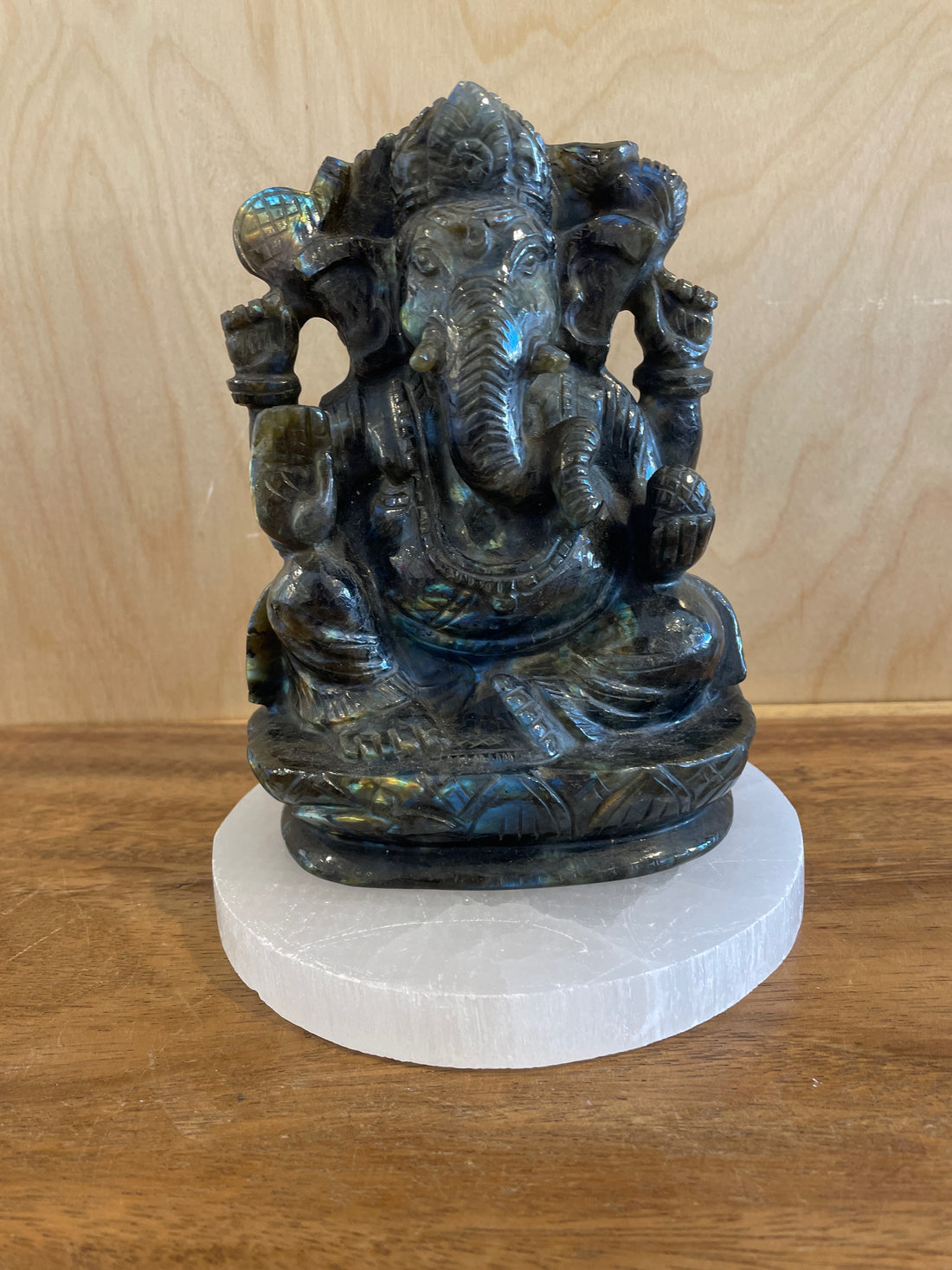 Labradorite statue of a ganesha on a white pedestal against a wooden background
