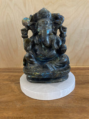 Labradorite statue of a ganesha on a white pedestal against a wooden background
