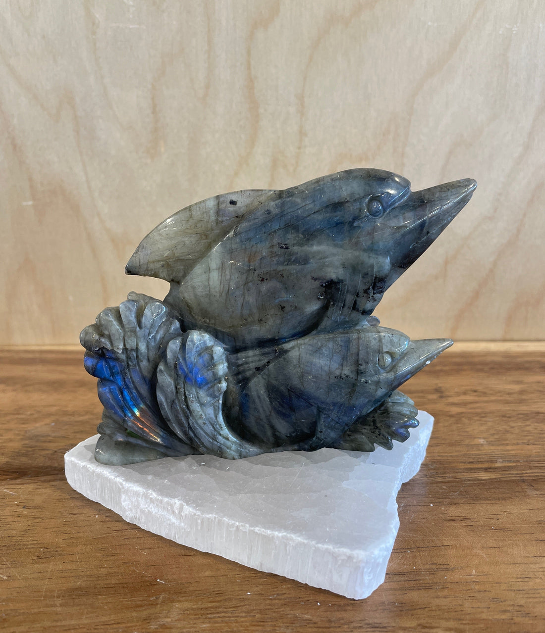 Stylized labradorite sculpture of two dolphins on a wooden surface