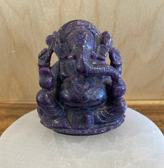 Purple crystal statue on a white stone base against a wooden background