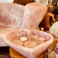 Rose quartz crystal bowl on a wooden stool with a pink crystal chair in the background.