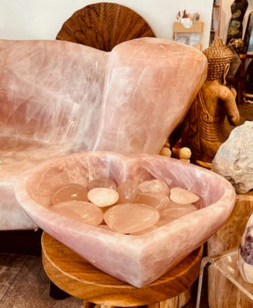 Rose quartz crystal bowl on a wooden stool with a pink crystal chair in the background.