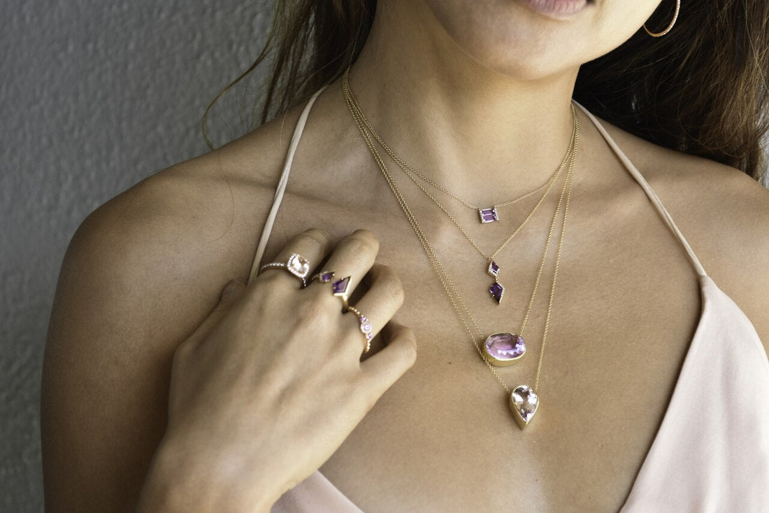 Woman wearing a 4 different necklaces with pink gemstones and rings on a neutral background