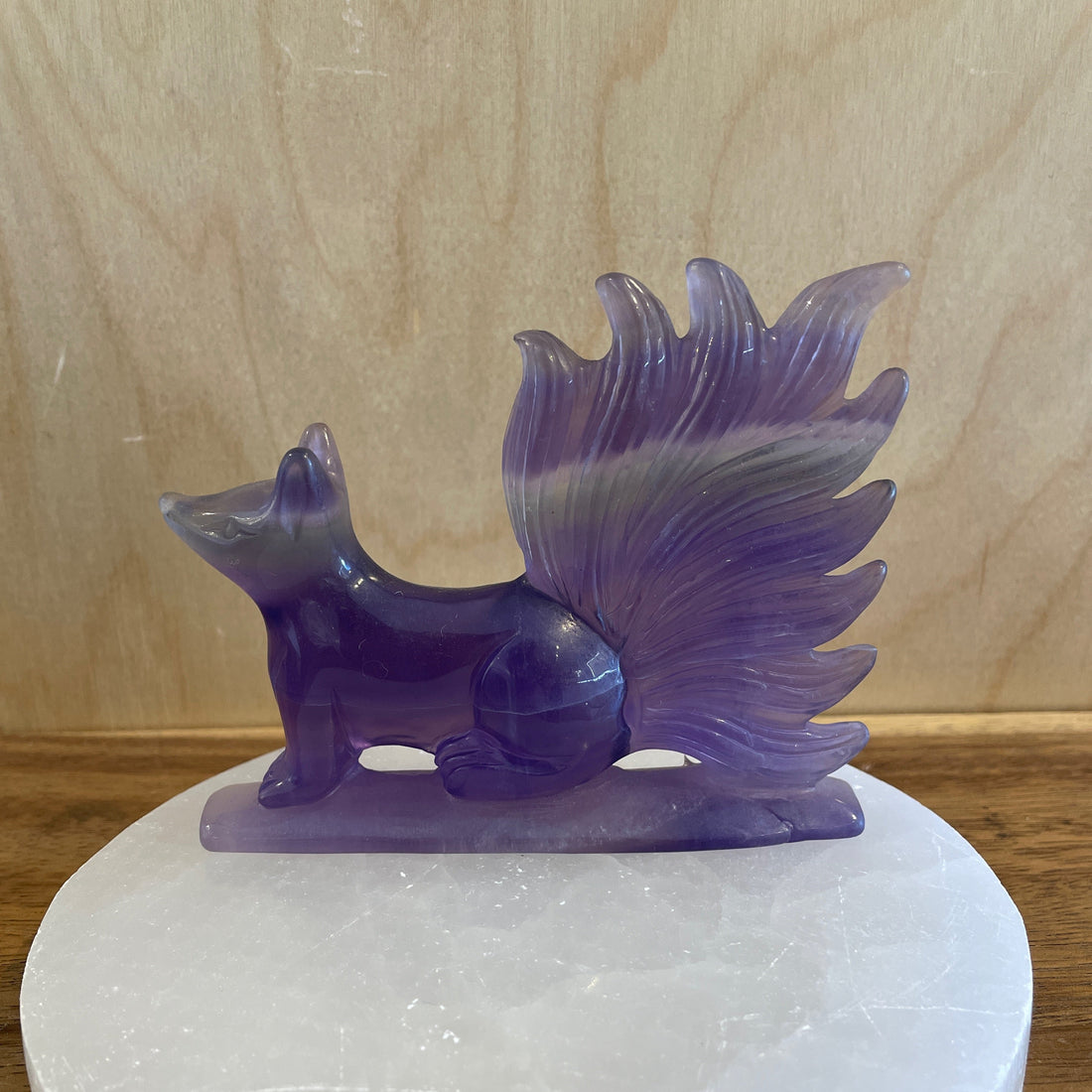 Purple fluorite crystal squirrel figurine on a white stone base against a wooden background