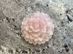 Pink quartz carved into a camellia like flower on a grey mottled background