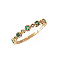 A gold band ring with multiple emerald gemstones set in it, alternating smaller diamonds.