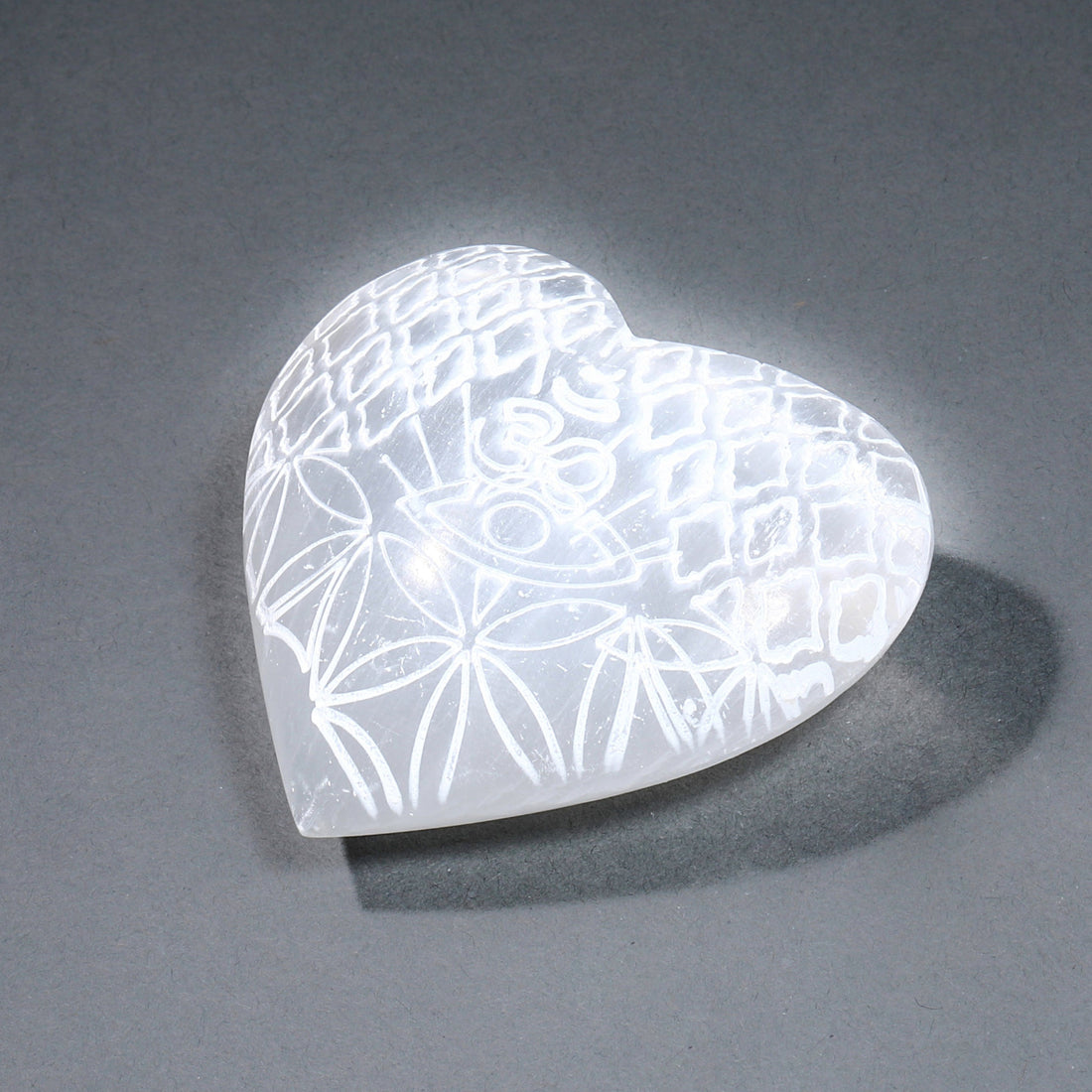 Heart-shaped selenite with etched pattern on a gray background