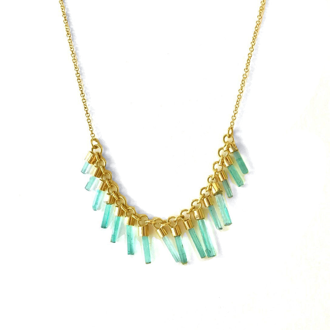 An 18k gold necklace with a series of columnar emeralds set in individual bezels, arranged in a line across the necklace.