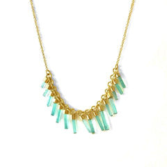 An 18k gold necklace with a series of columnar emeralds set in individual bezels, arranged in a line across the necklace.
